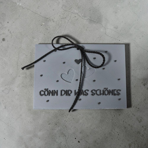 graue 3D Karte mit Schriftzug „Gönn dir was schönes“, Herz und dekorativen kleinen Herzen